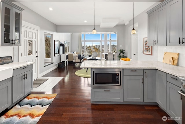 kitchen featuring stainless steel microwave, light stone counters, decorative light fixtures, and gray cabinets