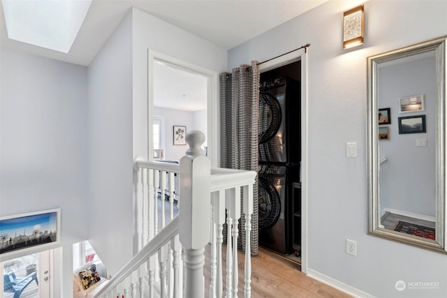 hall featuring stacked washer / drying machine, a skylight, and light hardwood / wood-style floors