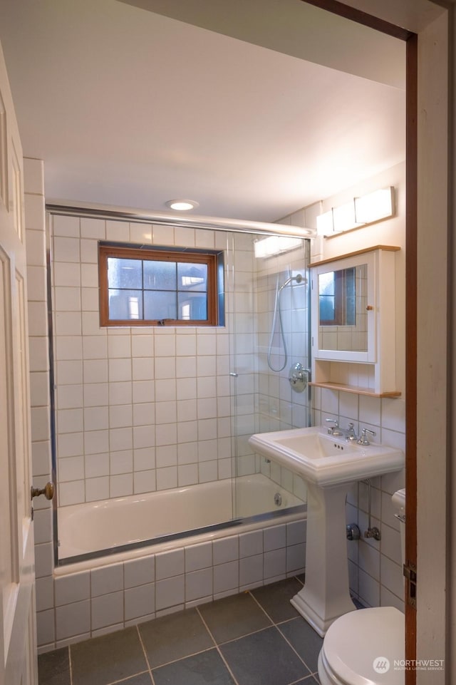 bathroom featuring toilet, bath / shower combo with glass door, and tile patterned flooring