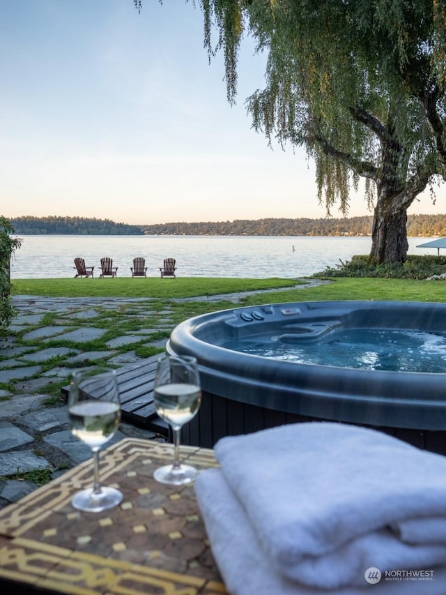 patio terrace at dusk with a water view and a hot tub