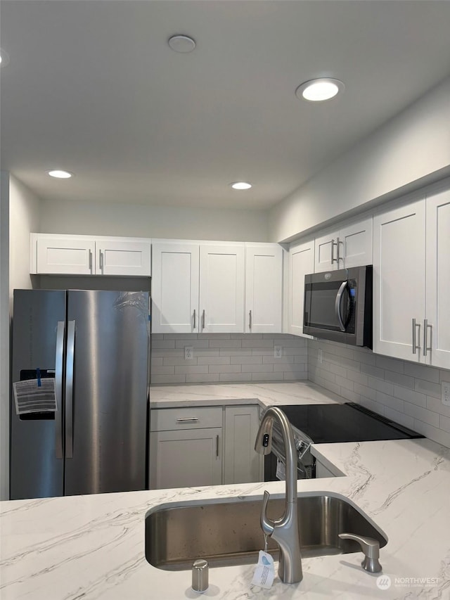 kitchen with sink, light stone countertops, white cabinets, and appliances with stainless steel finishes