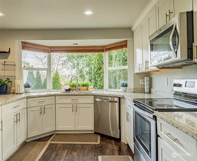 kitchen with dark wood-type flooring, sink, light stone counters, stainless steel appliances, and white cabinets