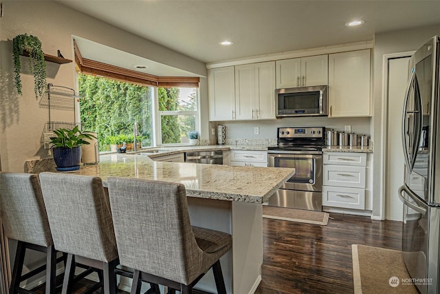 kitchen with sink, dark wood-type flooring, appliances with stainless steel finishes, white cabinetry, and kitchen peninsula