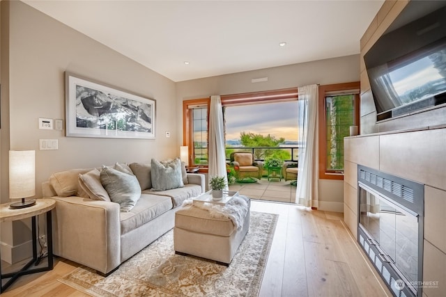 living room featuring light hardwood / wood-style flooring, a tiled fireplace, and plenty of natural light