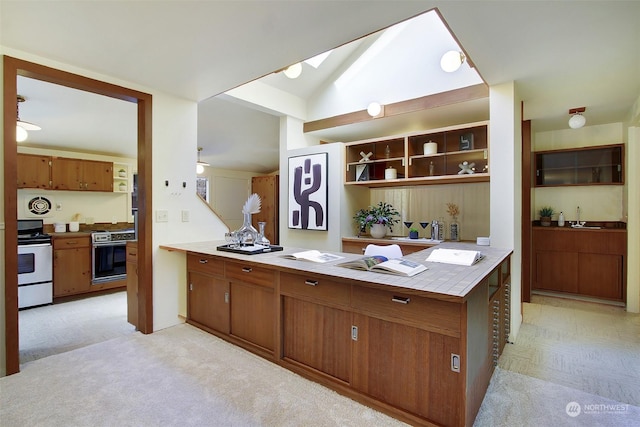 kitchen with sink, stainless steel range with electric cooktop, tile countertops, kitchen peninsula, and oven