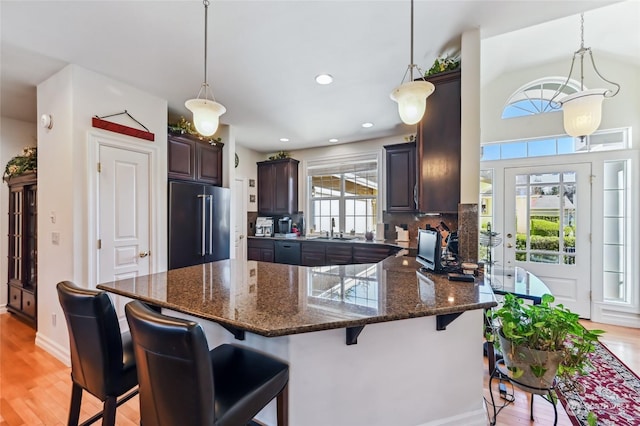 kitchen featuring a breakfast bar, high end fridge, sink, dark brown cabinets, and pendant lighting