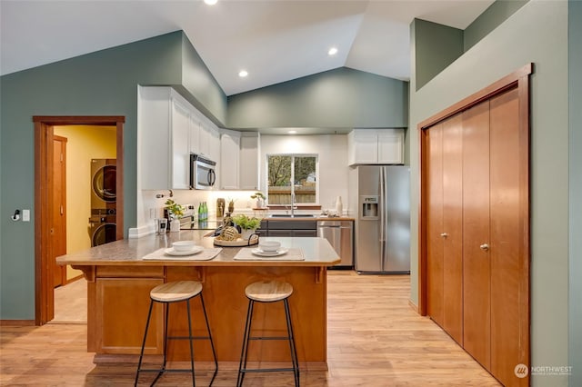 kitchen featuring stacked washing maching and dryer, a breakfast bar, white cabinetry, lofted ceiling, and stainless steel appliances