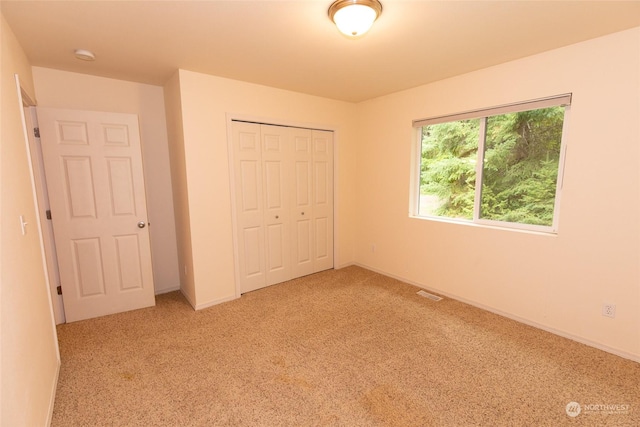 unfurnished bedroom with light colored carpet and a closet