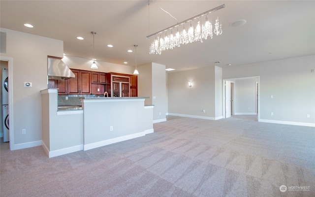 kitchen featuring tasteful backsplash, stacked washer / drying machine, light carpet, decorative light fixtures, and exhaust hood