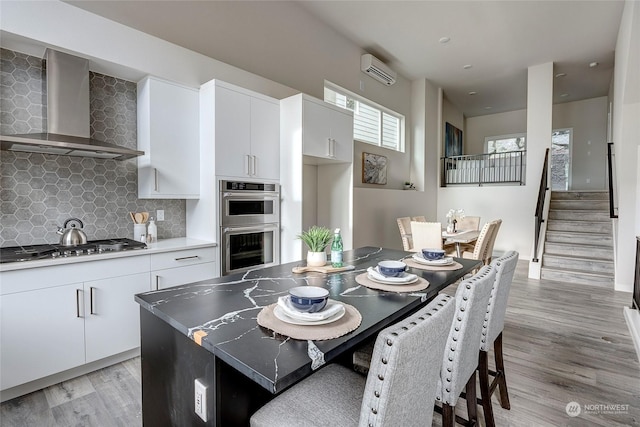 kitchen with white cabinetry, a kitchen island, backsplash, and wall chimney exhaust hood