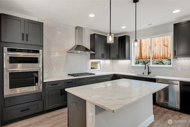 kitchen featuring sink, a center island, light hardwood / wood-style floors, stainless steel appliances, and wall chimney exhaust hood