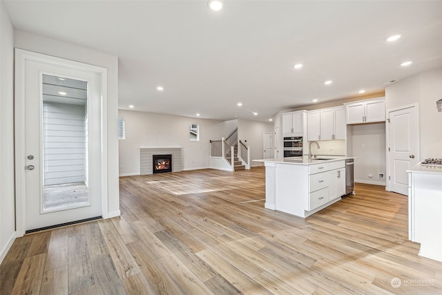 kitchen featuring dishwasher, white cabinetry, sink, a center island with sink, and light hardwood / wood-style flooring