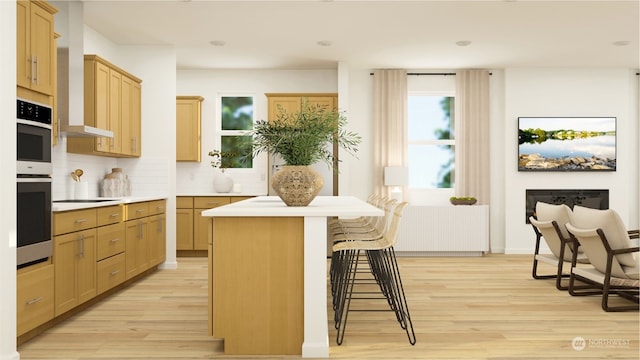 kitchen with a center island, light wood-type flooring, a kitchen breakfast bar, radiator, and backsplash