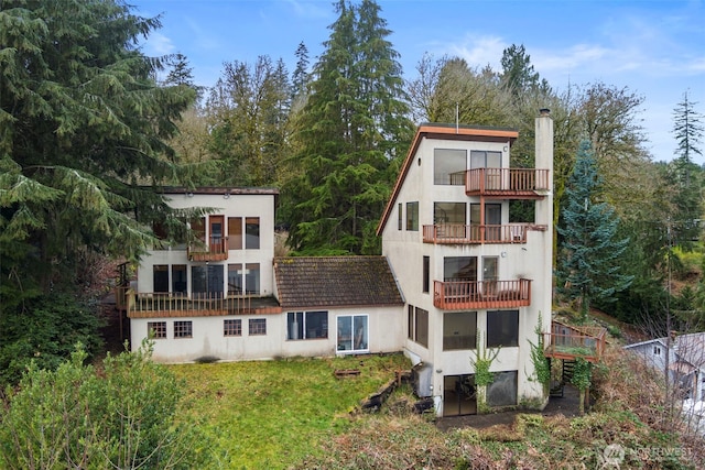 back of property featuring a lawn, a balcony, a chimney, central AC, and stucco siding