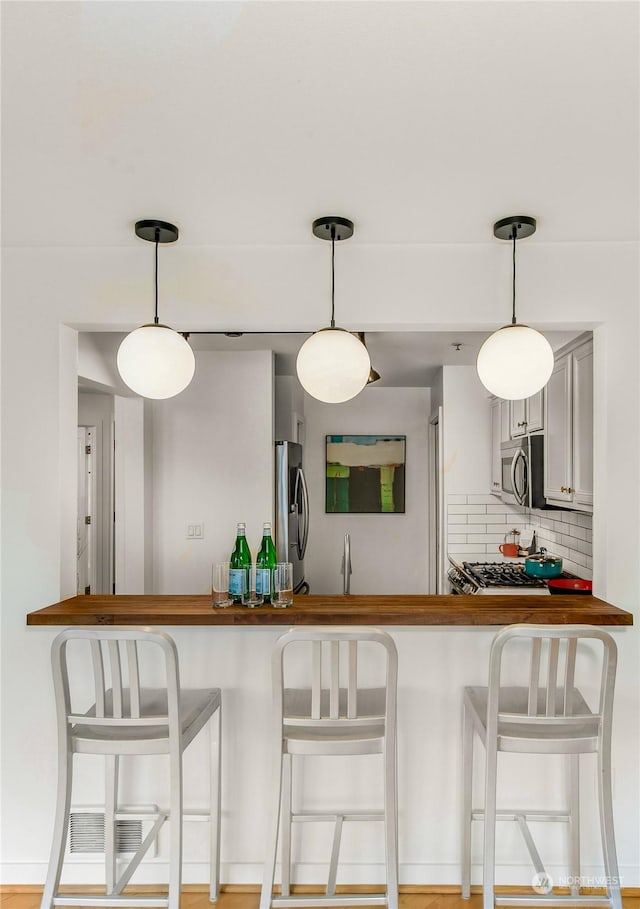 kitchen featuring stainless steel appliances, hanging light fixtures, backsplash, and a kitchen breakfast bar