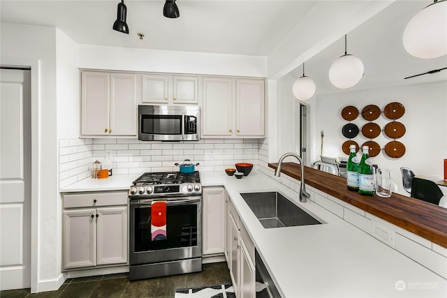 kitchen with pendant lighting, sink, backsplash, dark tile patterned flooring, and stainless steel appliances