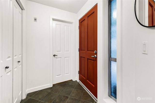 foyer with dark tile patterned flooring and baseboards