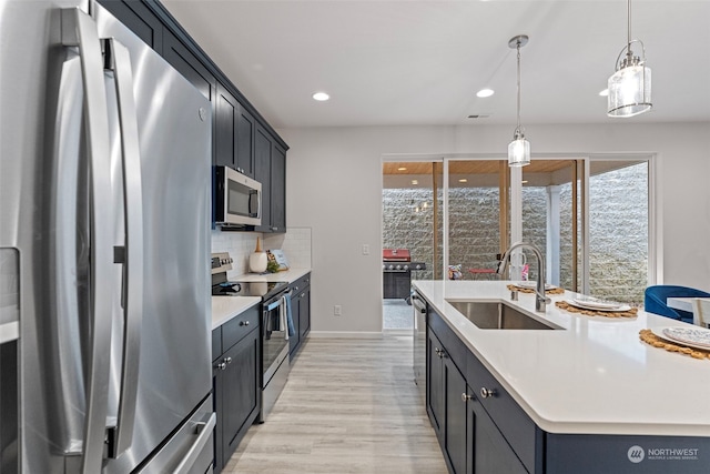 kitchen featuring pendant lighting, sink, appliances with stainless steel finishes, a kitchen island with sink, and tasteful backsplash