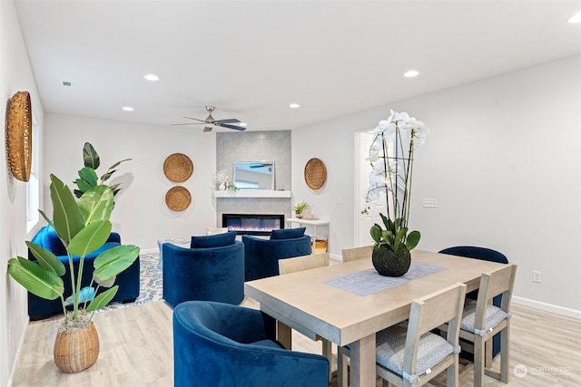 dining area with a tile fireplace, ceiling fan, and light hardwood / wood-style floors