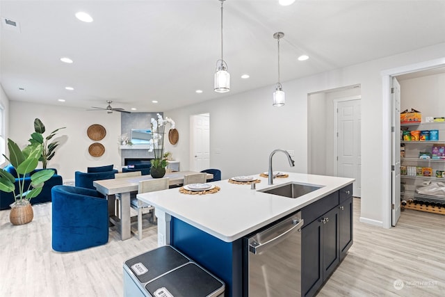 kitchen featuring sink, hanging light fixtures, dishwasher, a fireplace, and a kitchen island with sink