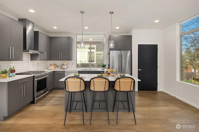 kitchen with gray cabinetry, high end appliances, decorative light fixtures, a center island, and wall chimney range hood