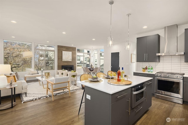 kitchen with a breakfast bar area, stainless steel appliances, a center island, decorative light fixtures, and wall chimney exhaust hood