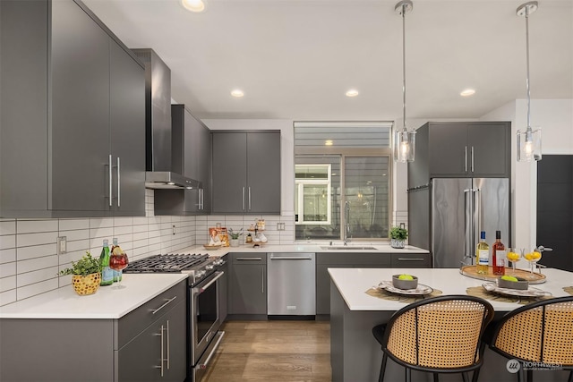 kitchen with wall chimney exhaust hood, sink, gray cabinetry, high end appliances, and hanging light fixtures