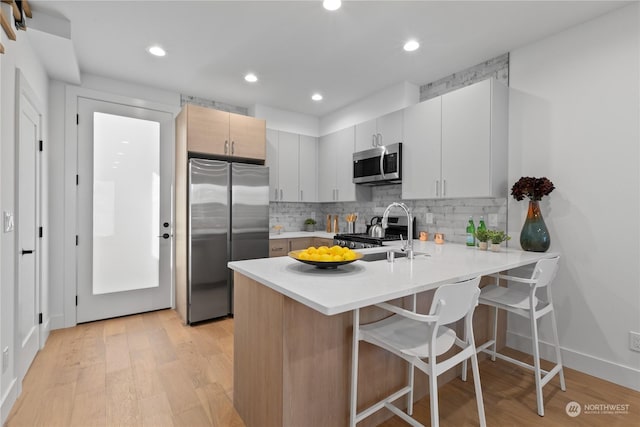 kitchen with a breakfast bar, sink, light hardwood / wood-style flooring, appliances with stainless steel finishes, and kitchen peninsula