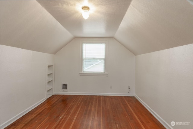 additional living space with heating unit, lofted ceiling, dark hardwood / wood-style flooring, a textured ceiling, and built in shelves