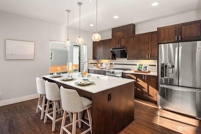 kitchen featuring sink, appliances with stainless steel finishes, backsplash, hanging light fixtures, and a center island with sink