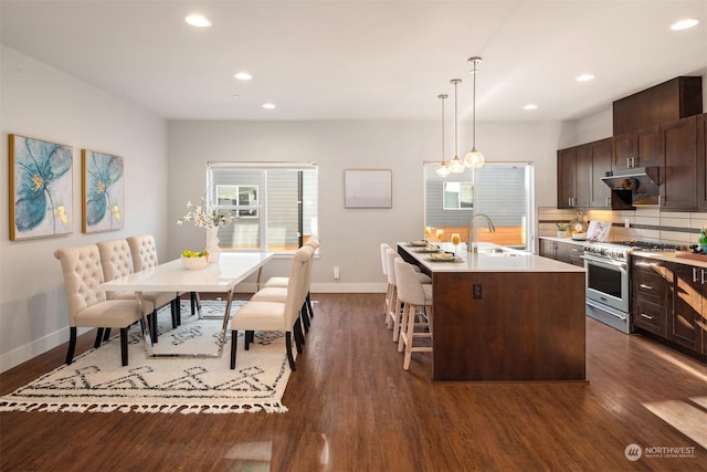 kitchen with sink, dark brown cabinets, a center island with sink, stainless steel stove, and pendant lighting