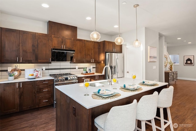 kitchen featuring appliances with stainless steel finishes, a kitchen breakfast bar, an island with sink, decorative backsplash, and decorative light fixtures