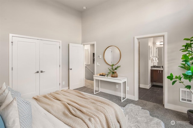 bedroom featuring dark carpet, ensuite bath, a closet, and a towering ceiling