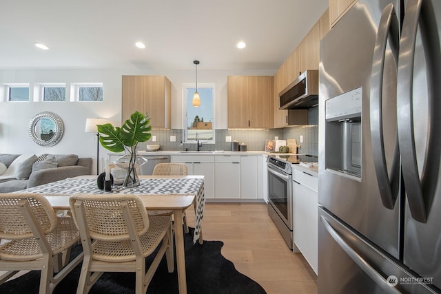 kitchen with sink, appliances with stainless steel finishes, hanging light fixtures, backsplash, and white cabinets