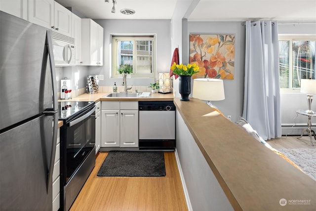 kitchen featuring appliances with stainless steel finishes, sink, white cabinets, a baseboard heating unit, and light wood-type flooring