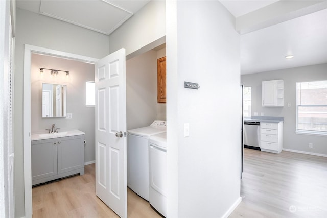 laundry room featuring washer and dryer, sink, cabinets, and light wood-type flooring