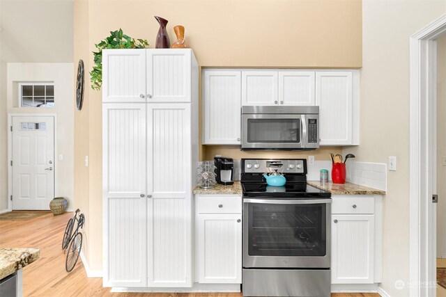 kitchen with appliances with stainless steel finishes, light stone countertops, light hardwood / wood-style flooring, and white cabinets