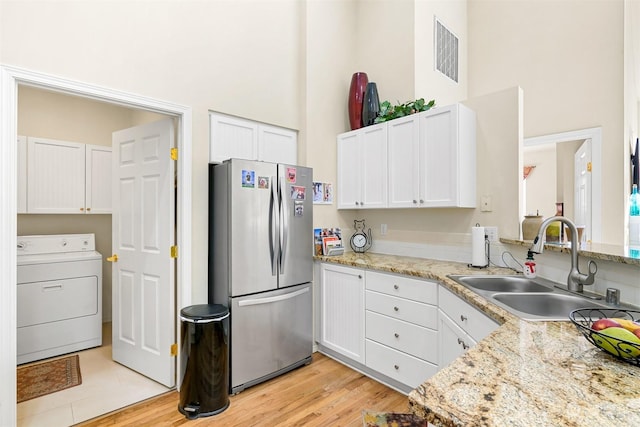 kitchen with stainless steel refrigerator, washer / dryer, sink, white cabinets, and light hardwood / wood-style flooring