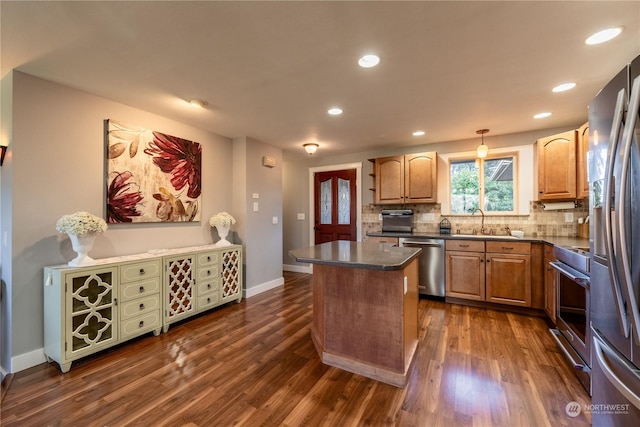 kitchen with stainless steel appliances, dark countertops, a sink, and a kitchen island