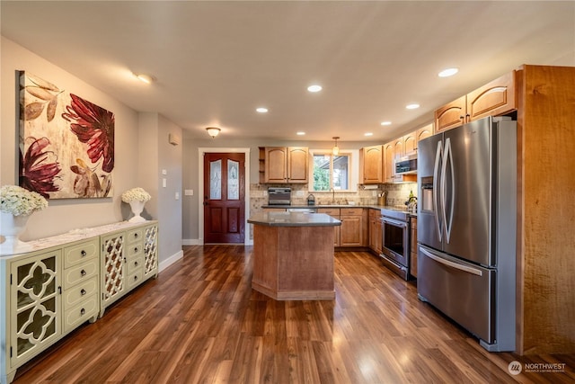 kitchen with appliances with stainless steel finishes, dark wood finished floors, a sink, and tasteful backsplash