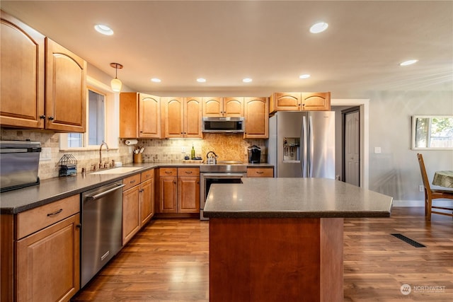 kitchen with appliances with stainless steel finishes, dark wood-type flooring, a sink, and backsplash