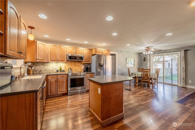 kitchen featuring tasteful backsplash, dark countertops, a kitchen island, appliances with stainless steel finishes, and a sink