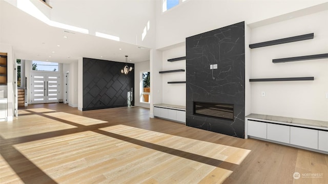 unfurnished living room with a fireplace, a wealth of natural light, a high ceiling, and light wood-type flooring