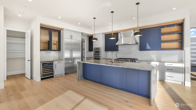 kitchen with backsplash, beverage cooler, hanging light fixtures, and wall chimney range hood