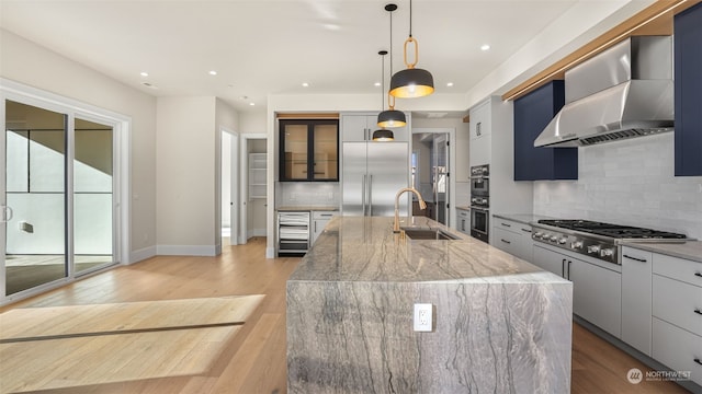 kitchen featuring sink, a large island, stainless steel appliances, light stone countertops, and wall chimney range hood