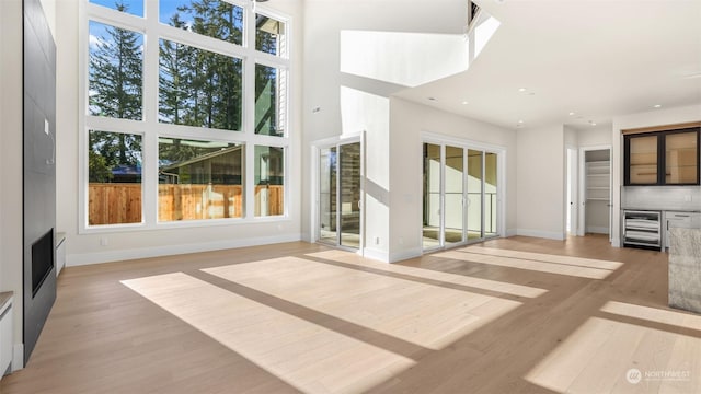 unfurnished living room featuring a high ceiling, wine cooler, and light hardwood / wood-style floors