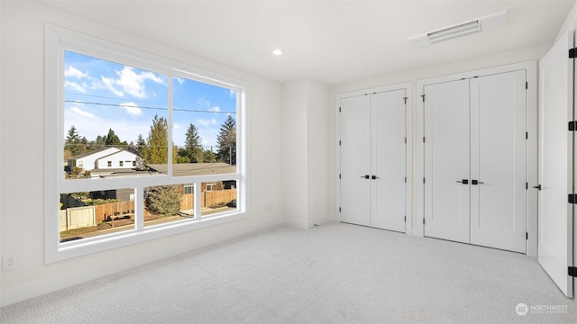 unfurnished bedroom featuring two closets and light colored carpet