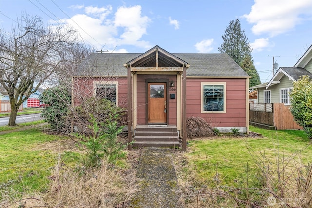 bungalow-style house with a shingled roof, fence, and a front lawn