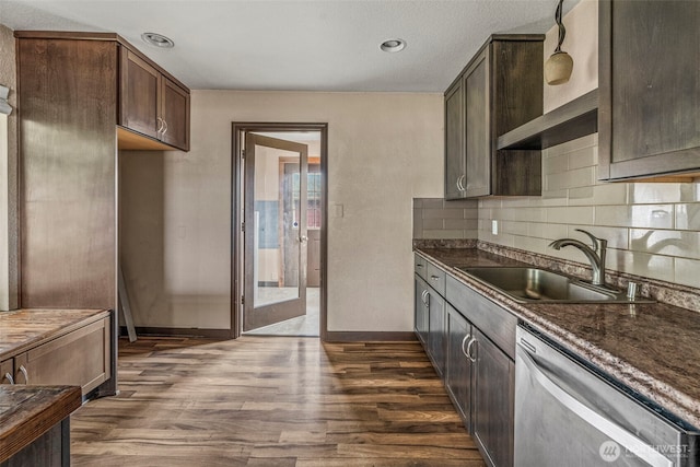 kitchen with hanging light fixtures, stainless steel dishwasher, dark wood-type flooring, a sink, and dark stone counters