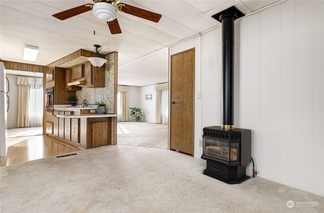 interior space with ceiling fan, wooden walls, sink, and a wood stove